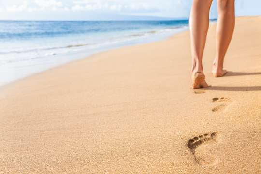 Beach travel - woman relaxing walking on sand beach leaving footprints in the sand. Closeup detail of female feet and legs on golden sand on Kaanapali beach, Maui, Hawaii, USA.