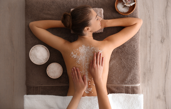 Young woman having body scrubbing procedure with sea salt in spa salon, top view